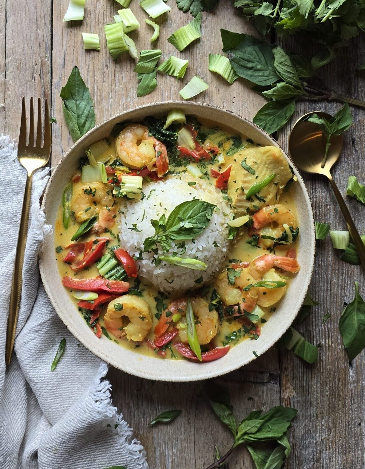 A bowl of Thai Fish Curry and rice sits on the table, with fresh cilantro and basil leaves to the side.