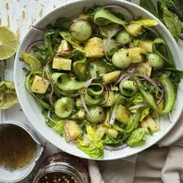 A bowl of Pineapple Cucumber Salad with Mint sits on the table, with hot Honey vinaigrette to the side.