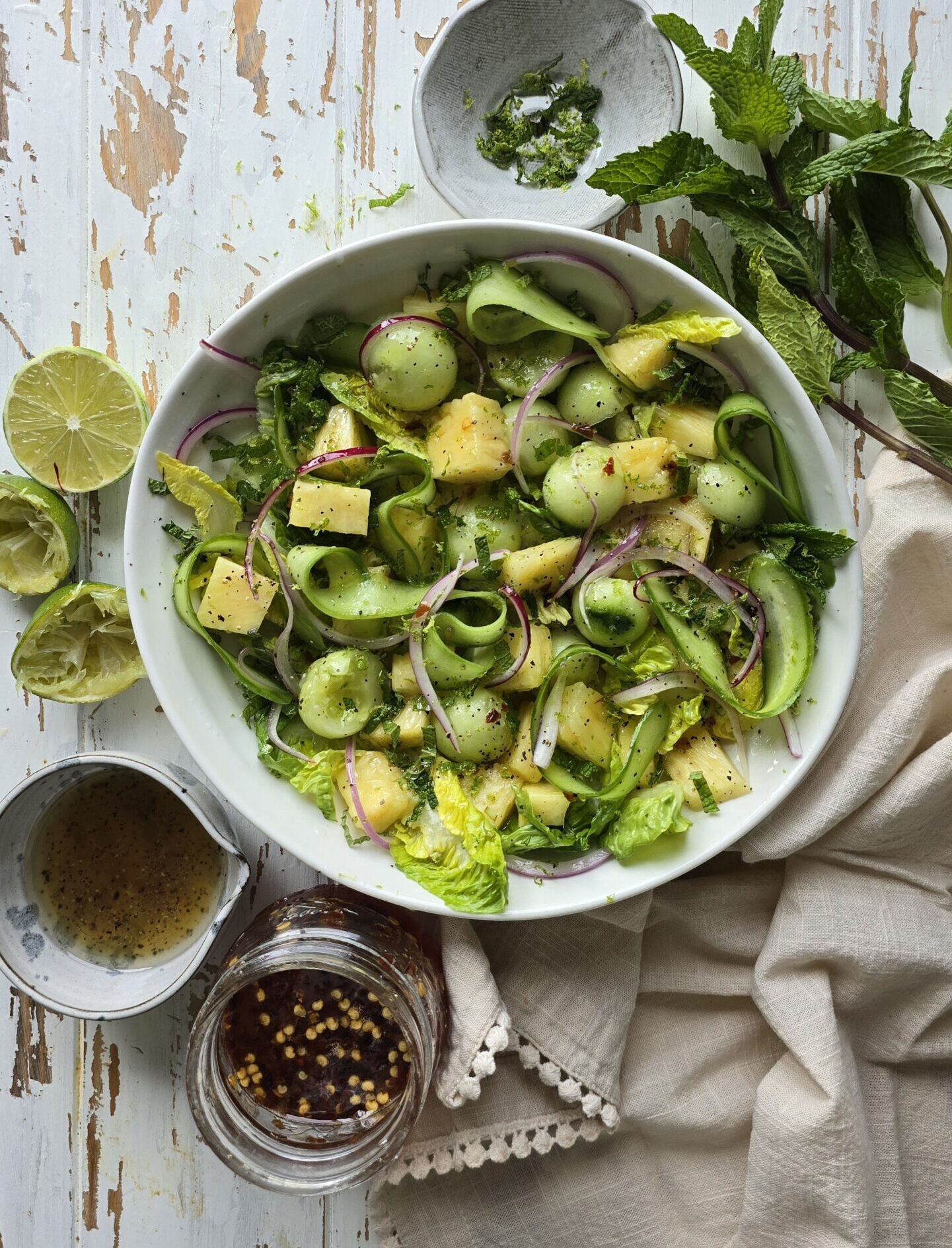 A bowl of Pineapple Cucumber Salad with Mint sits on the table, with hot Honey vinaigrette to the side.