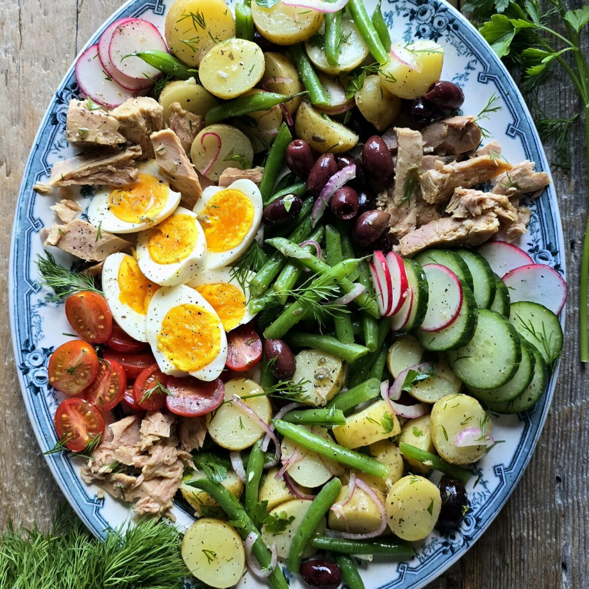 A platter filled with Nicoise Potato Salad and all the other fixings of a Nicoise Salad sits on the table ready to be enjoyed.