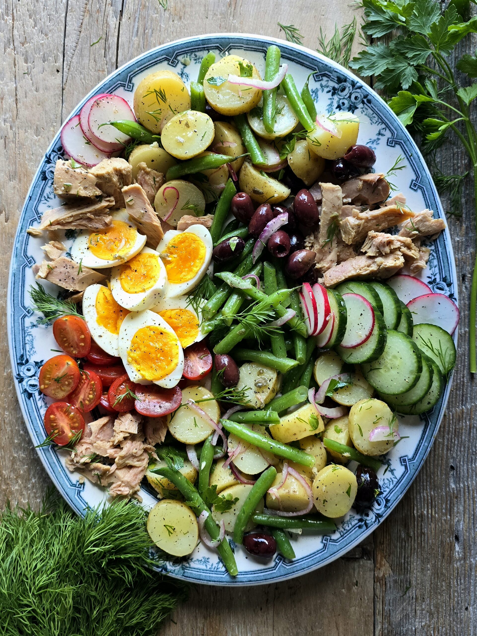 A platter filled with Nicoise Potato Salad and all the other fixings of a Nicoise Salad sits on the table ready to be enjoyed.