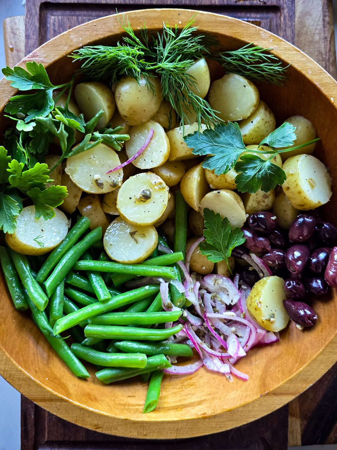 The ingredients for a Niçoise Potato Salad are in the bowl ready to be tossed.