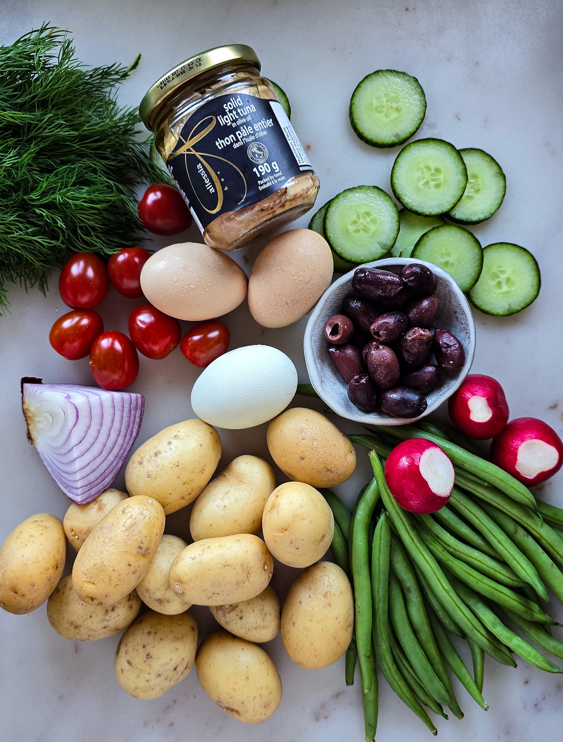 Ingredients needed to make a Niçoise Potato Salad are on the counter ready to be used.