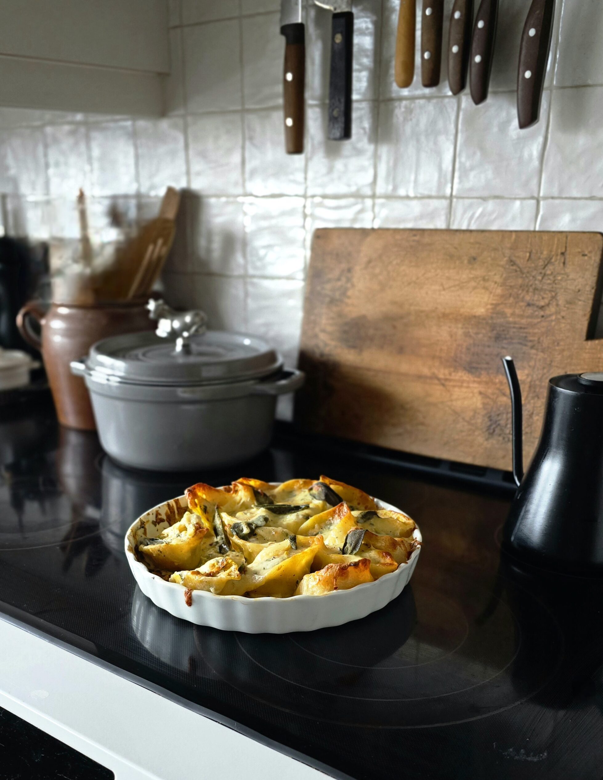 A baking dish filled with cheesy, baked Squash, Kale and Sausage Stuffed Shells sits on the stove.