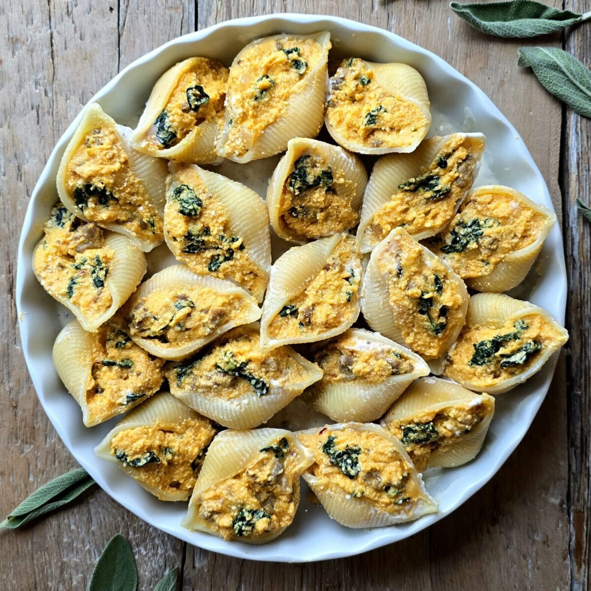 A baking dish filled with Squash, Kale and Sausage Stuffed Pasta Shells sits on the counter with sage leaves to the side.