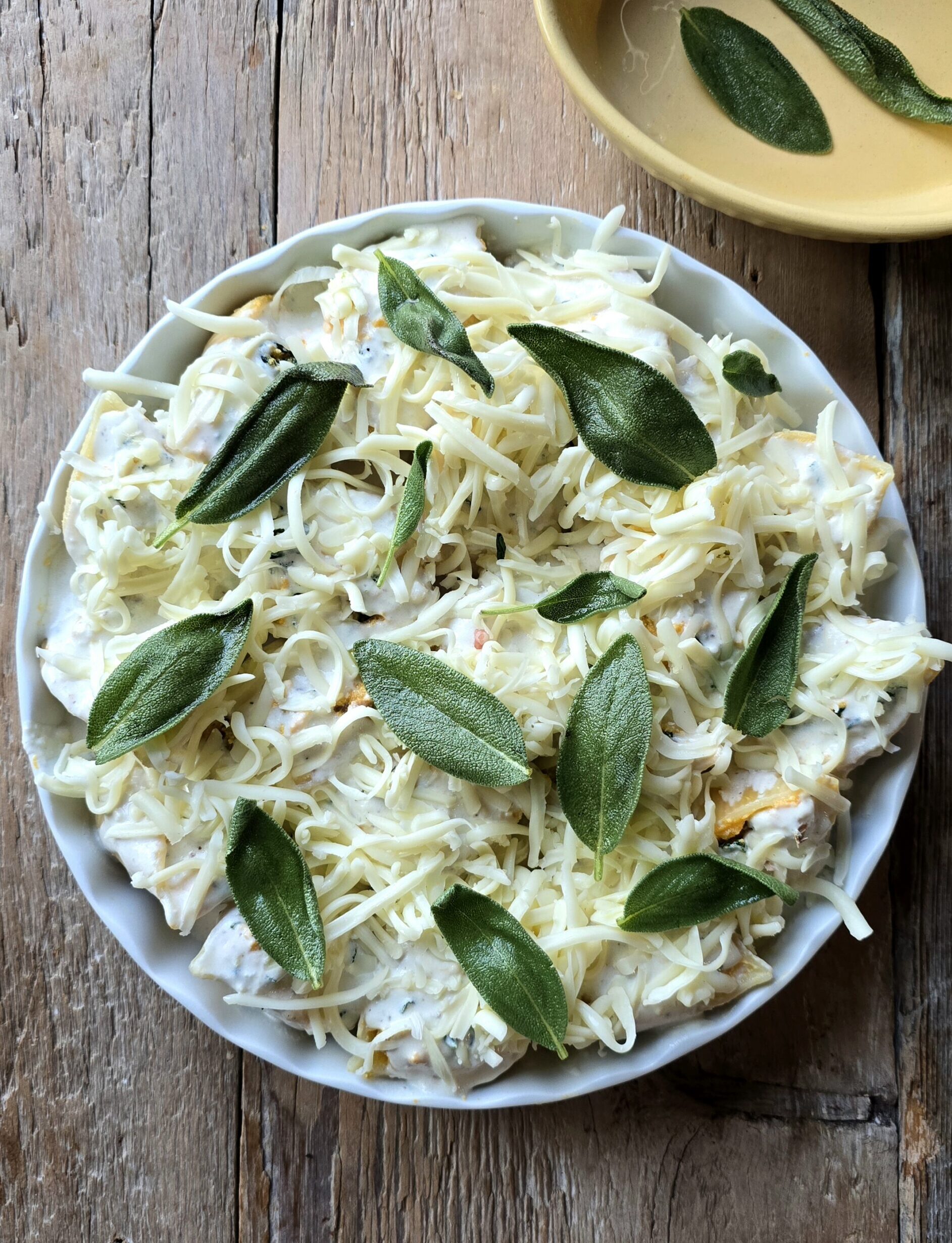 A baking dish filled with Squash, Kale and Sausage Stuffed Shells is covered with Sage Bechamel Sauce and shredded mozzarella cheese.