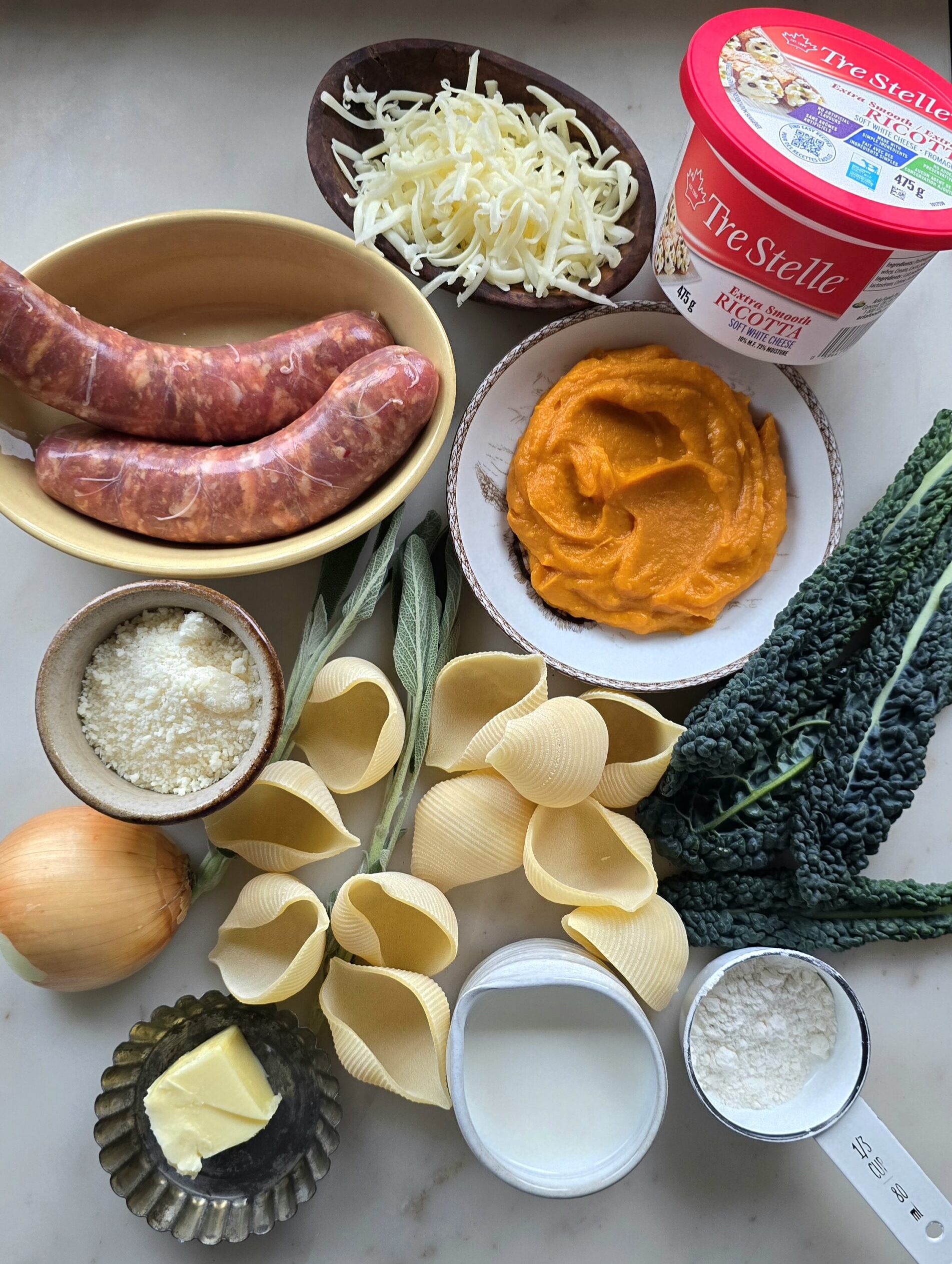 The ingredients needed to make Squash, Kale and Sausage Stuffed Shells are spread out on the counter.