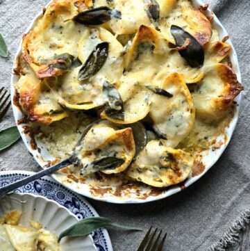 A dish filled with baked Squash, Kale and Sausage Stuffed Shells is being served out, with one plate containing gooey cheese covered shells to the side.