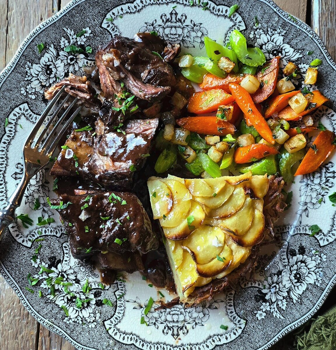 A dinner plate is loaded with braised short ribs, pan roasted vegetables and a slice of Potato Pie.