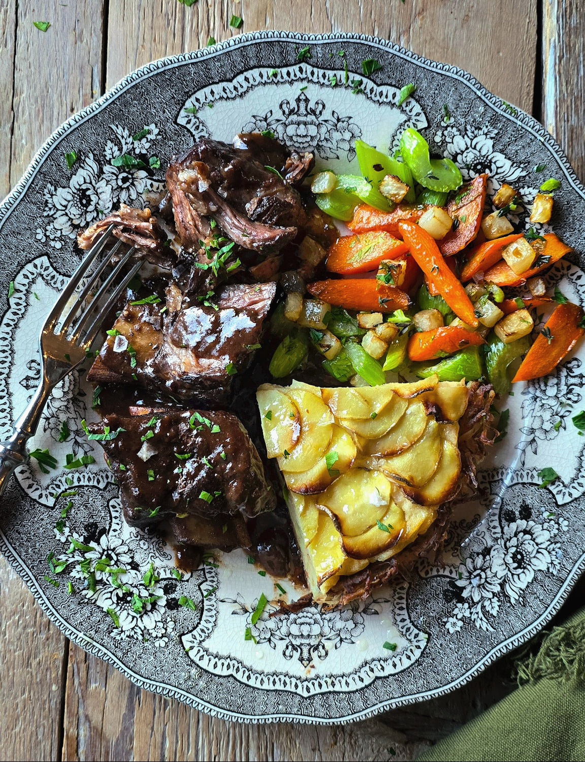 A dinner plate is loaded with braised short ribs, pan roasted vegetables and a slice of Potato Pie.
