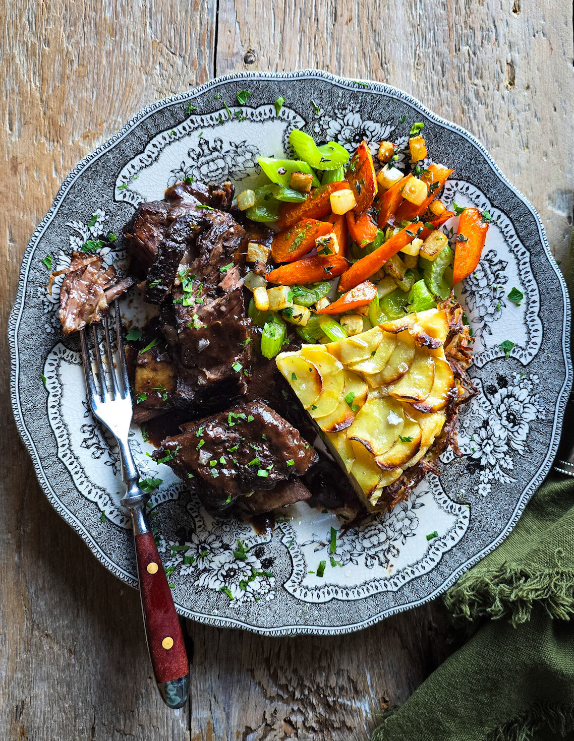 A dinner plate is loaded with braised short ribs, pan roasted vegetables and a slice of Potato Pie.