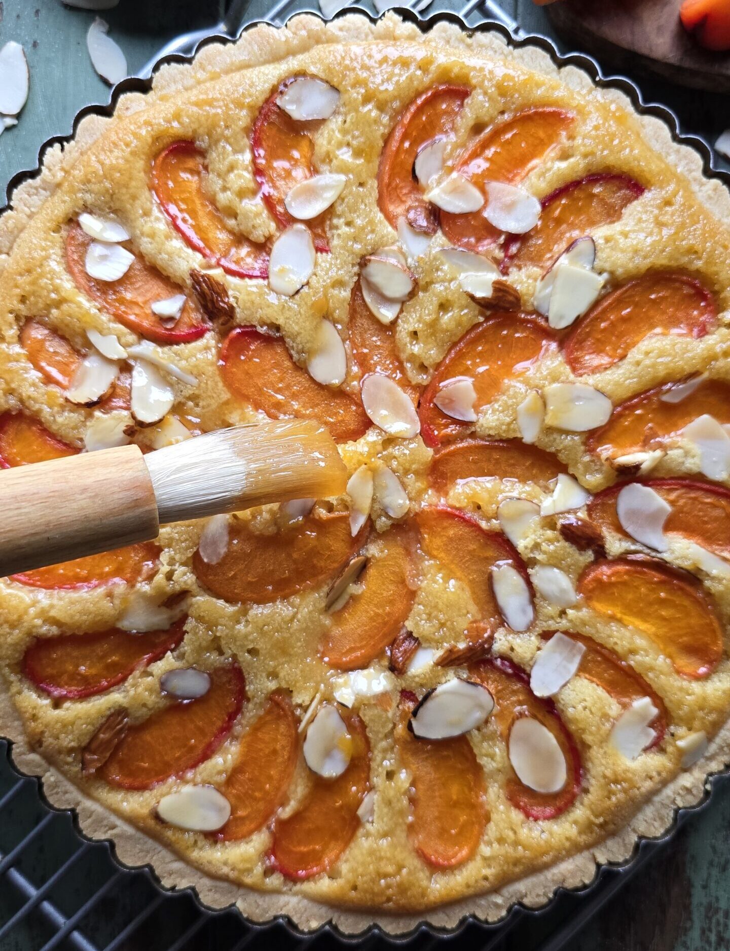 Brushing a freshly baked Apricot Frangipane Tart with warmed through apricot jam.