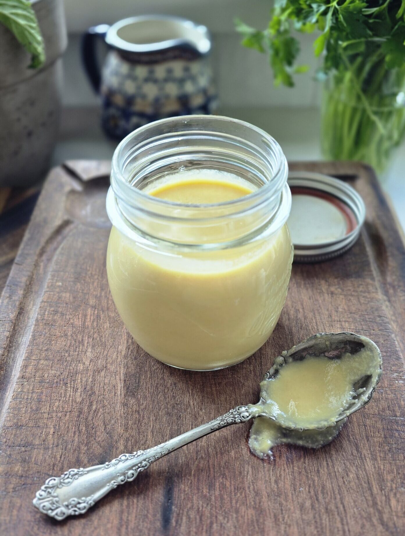 A jar of vanilla Creme Anglaise sits on the counter with a spoonful to the side.